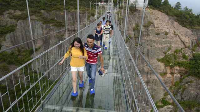 Varios turistas cruzan la pasarela de vidrio del parque Shiniuzhai en China.