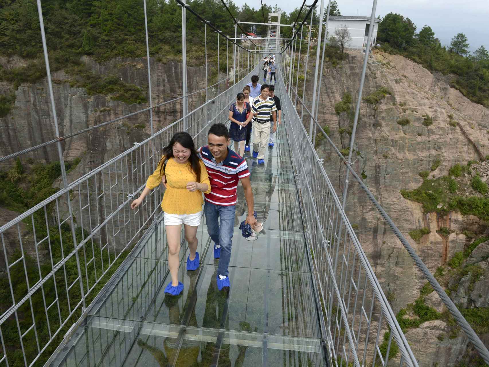 Varios turistas cruzan la pasarela de vidrio del parque Shiniuzhai en China.