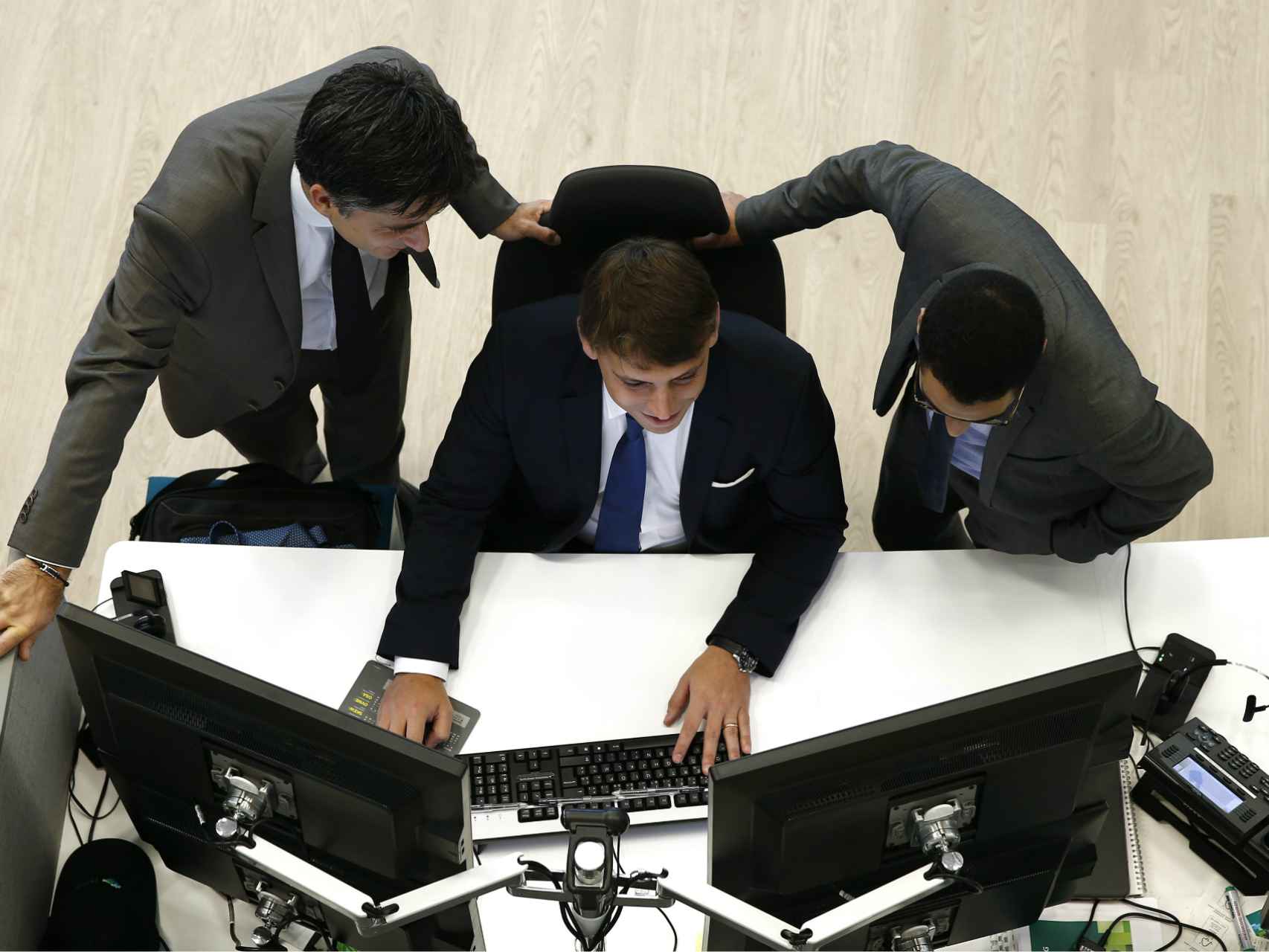 Tres operadores observan sus pantallas de cotizaciones.