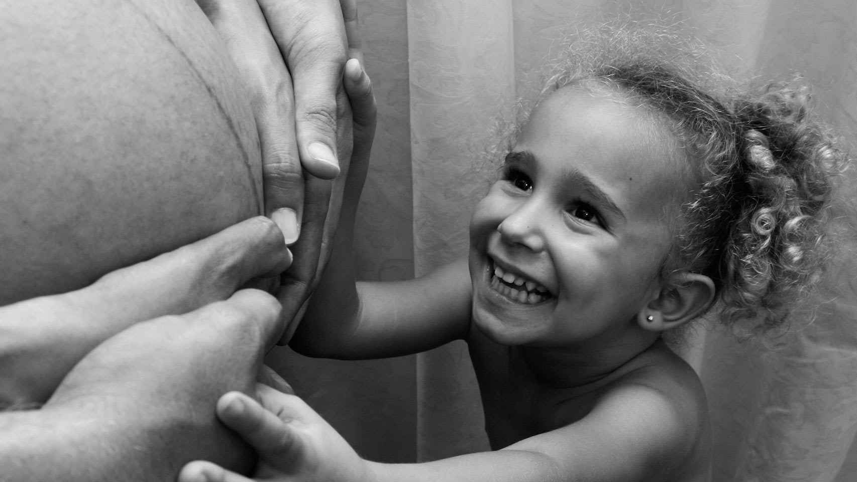Una niña toca la tripa de una mujer embarazada.