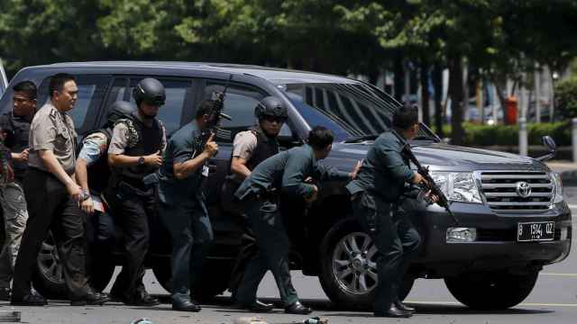 Agentes de la Policía indonesa avanzan con rifles y resguardados tras un coche.