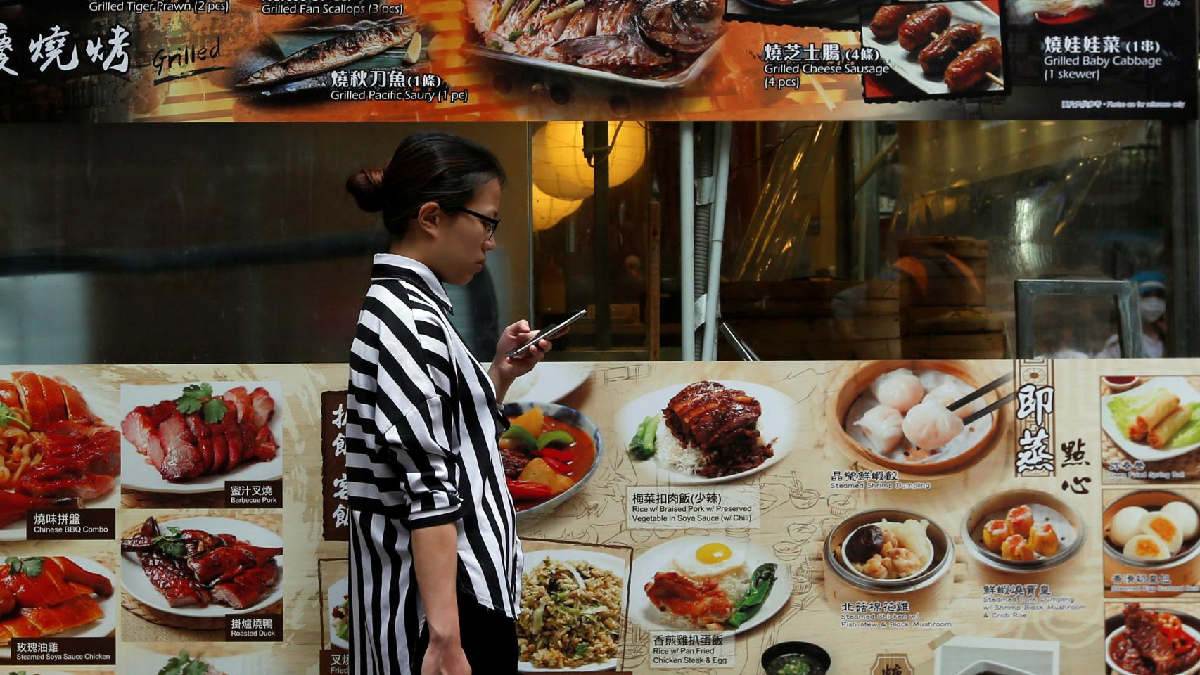 A woman checks her smartphone outside a restaurant at Tsim Sha Tsui shopping district in Hong Kong