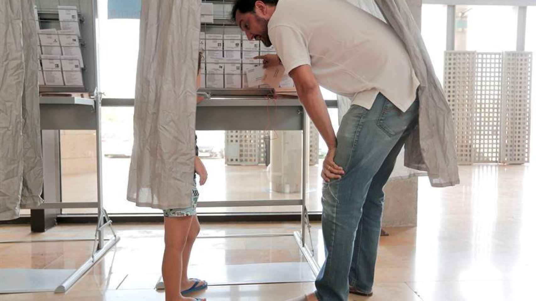 Un hombre muestra a su hijo las papeletas de los diferentes partidos.