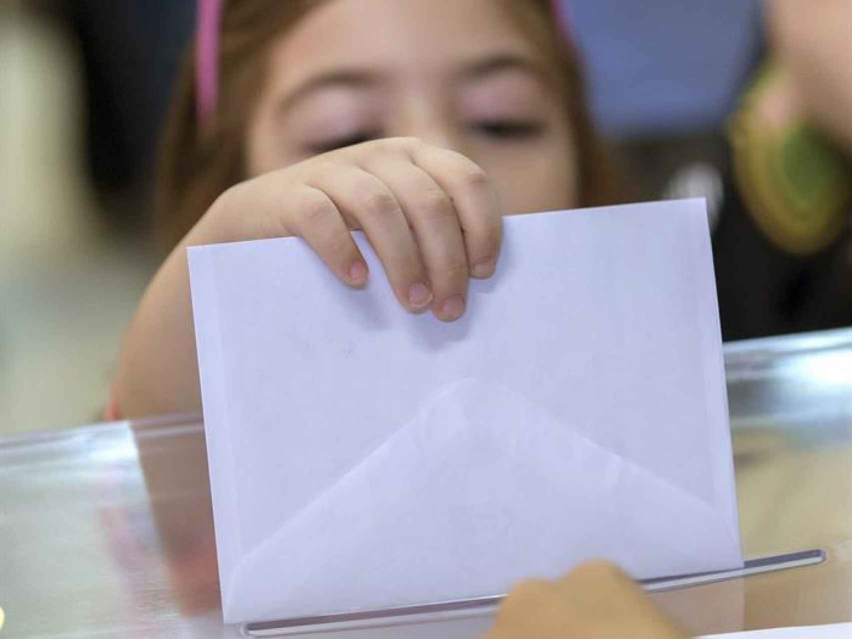 Una niña intenta introducir el sobre en la urna con el voto de su madre para el Senado este mediodía en un colegio electoral del barrio de Triana en Sevilla.