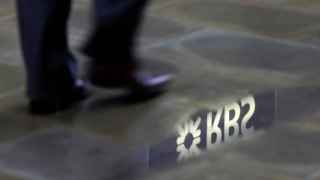 A man walks past a  Royal Bank of Scotland branch reflected in a puddle in central London