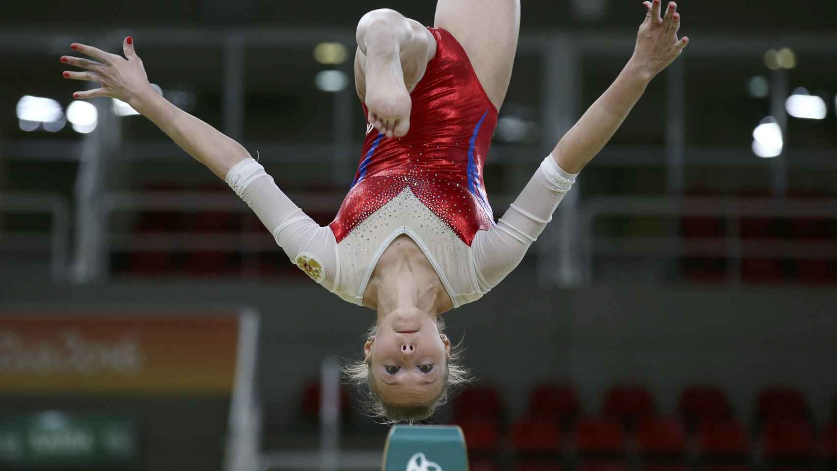 Una gimnasta realiza un mortal hacia atrás en barra equilibrio-