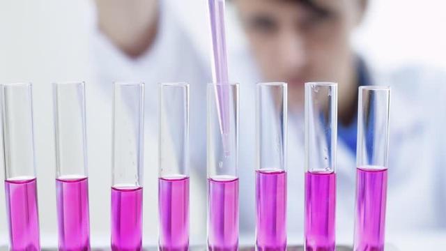 Una científica echa un líquido, por supuesto rosa, en pipetas.