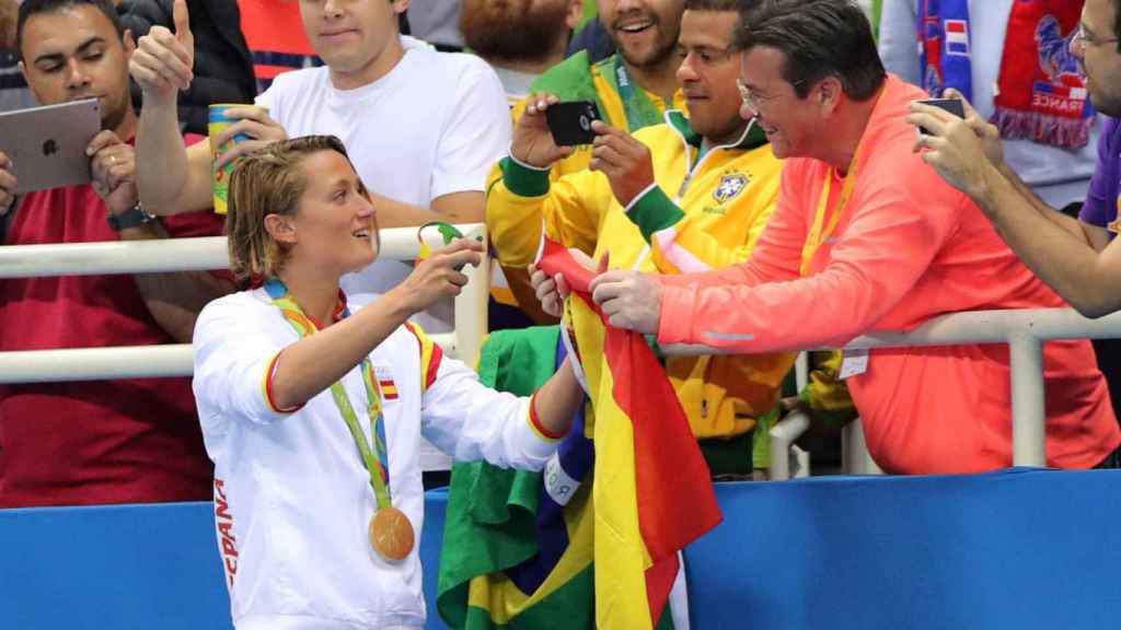 La deportista saluda a su padre, que le ofrece la bandera de España.