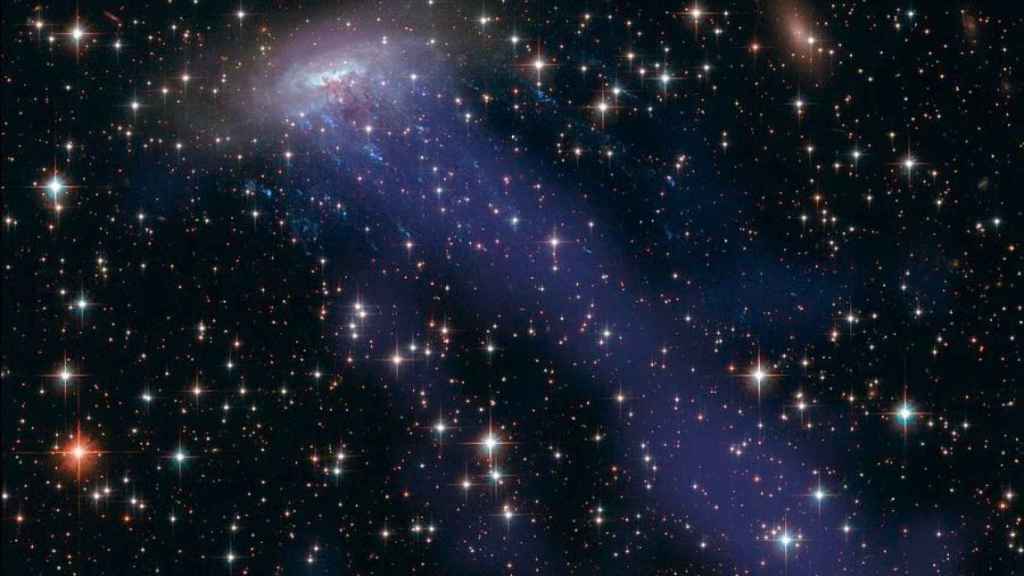 Recreación artística del mecanismo Ram pressure stripping dejando un rastro de gas (en color azul) en la galaxia ESO 137-001.