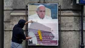 Un trabajador cubre un cartel publicitario contra el Papa colgado ilegalmente.