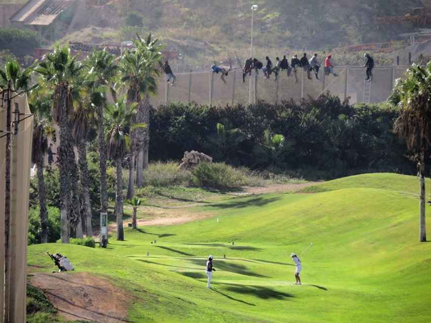 Inmigrantes encaramados en la verja de Melilla frente a golfistas en octubre de 2014.