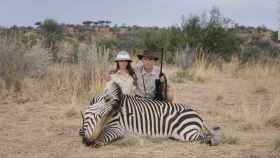 Dos turistas posan con una cebra recién cazada en Safari.