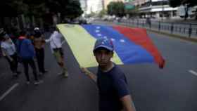 Un opositor enarbola una bandera venezolana en una avenida