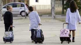 Tres niños con sus maletines escolares se dirigen al colegio.
