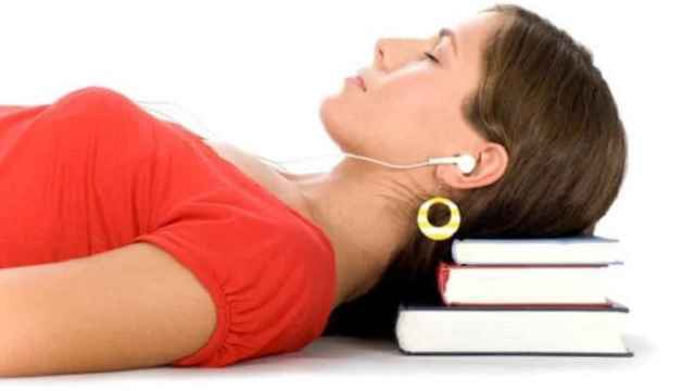 Una mujer duerme apoyada en unos libros con los auriculares puestos.