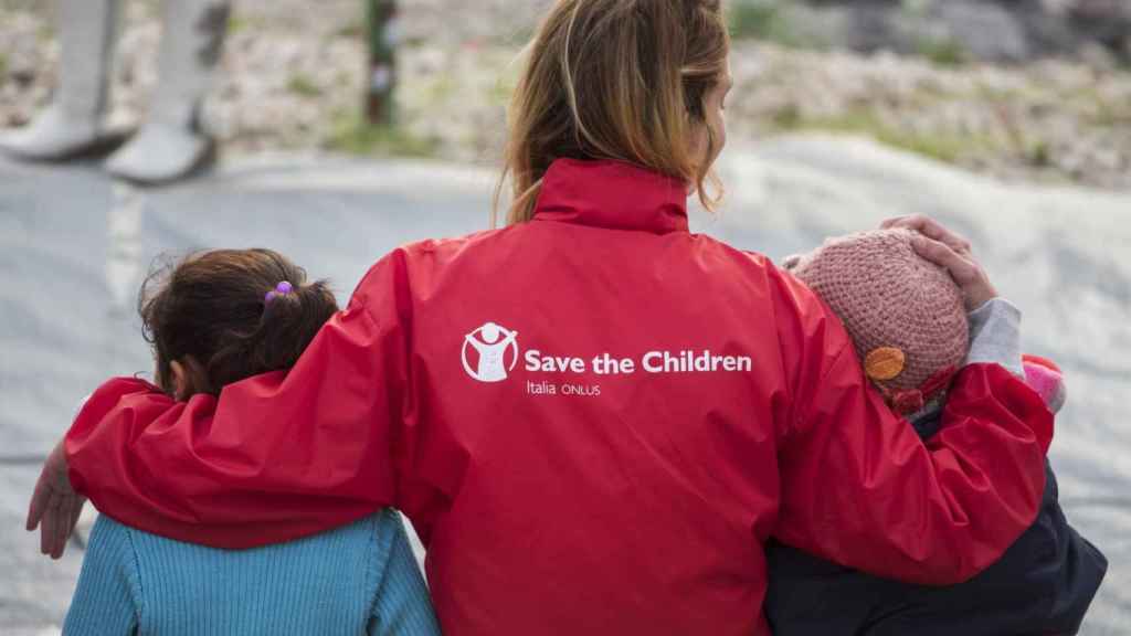 Dos niños acompañados de una voluntaria de The Save The Children