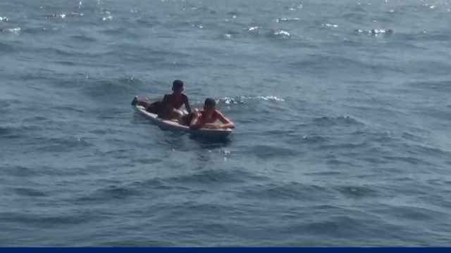 Dos inmigrantes cruzando en una tabla de surf el estrecho.