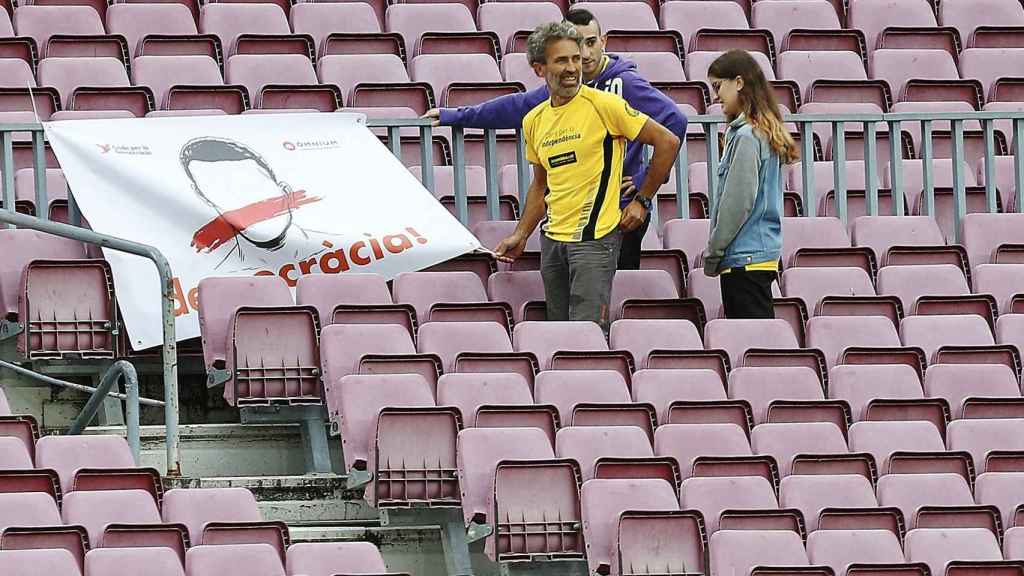 Tres espectadores en las gradas del Camp Nou con una pancarta.