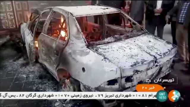 Las personas se paran cerca de un automóvil en llamas en Zanjan, Irán.