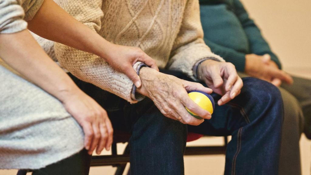 Una persona acompaña a un anciano que sujeta una pelota.