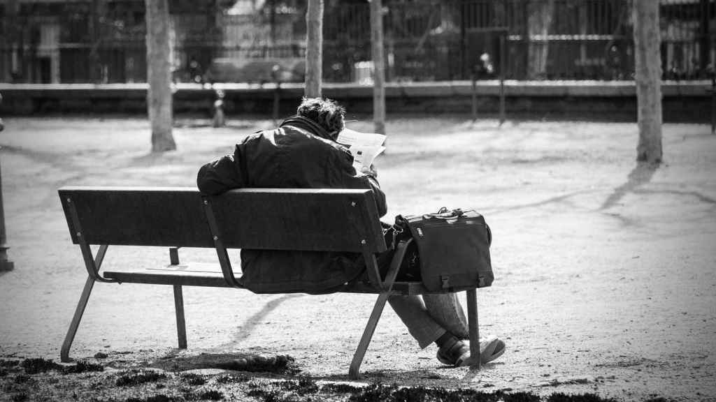 Un anciano lee solo el periódico en el banco de un parque.