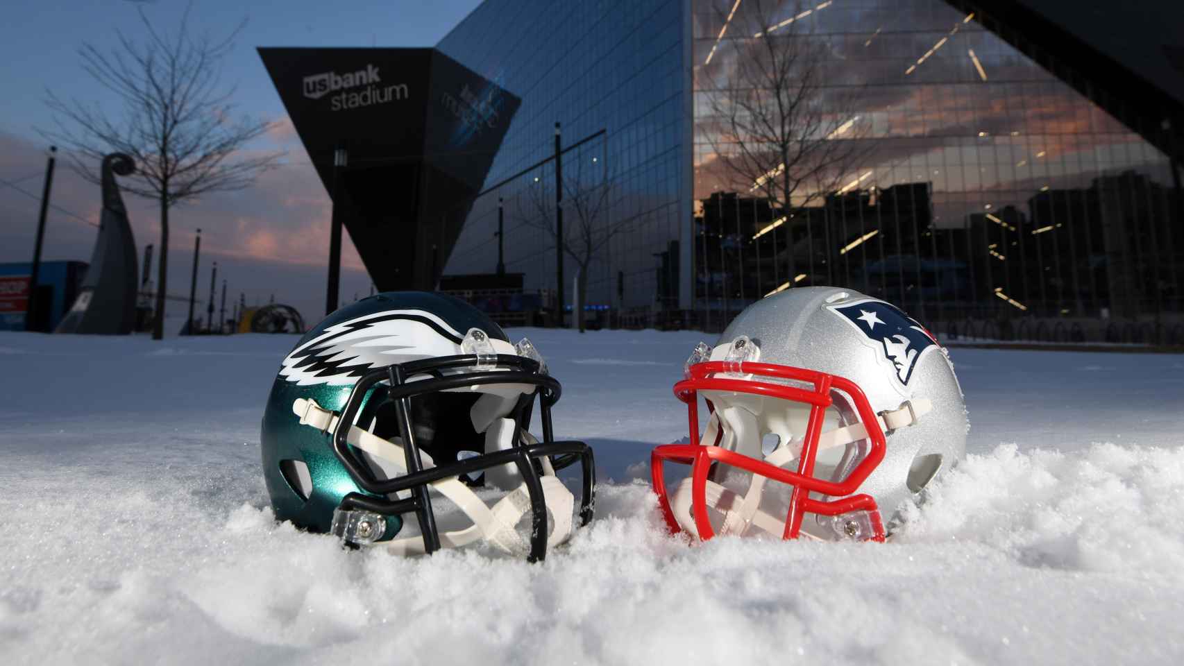 Exterior del US Bank Stadium, con los cascos de Patriots y Eagles sobre la nieve.