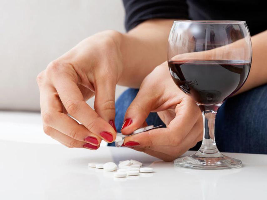 Una persona dispuesta a tomarse una copita de vino junto con algunos medicamentos.