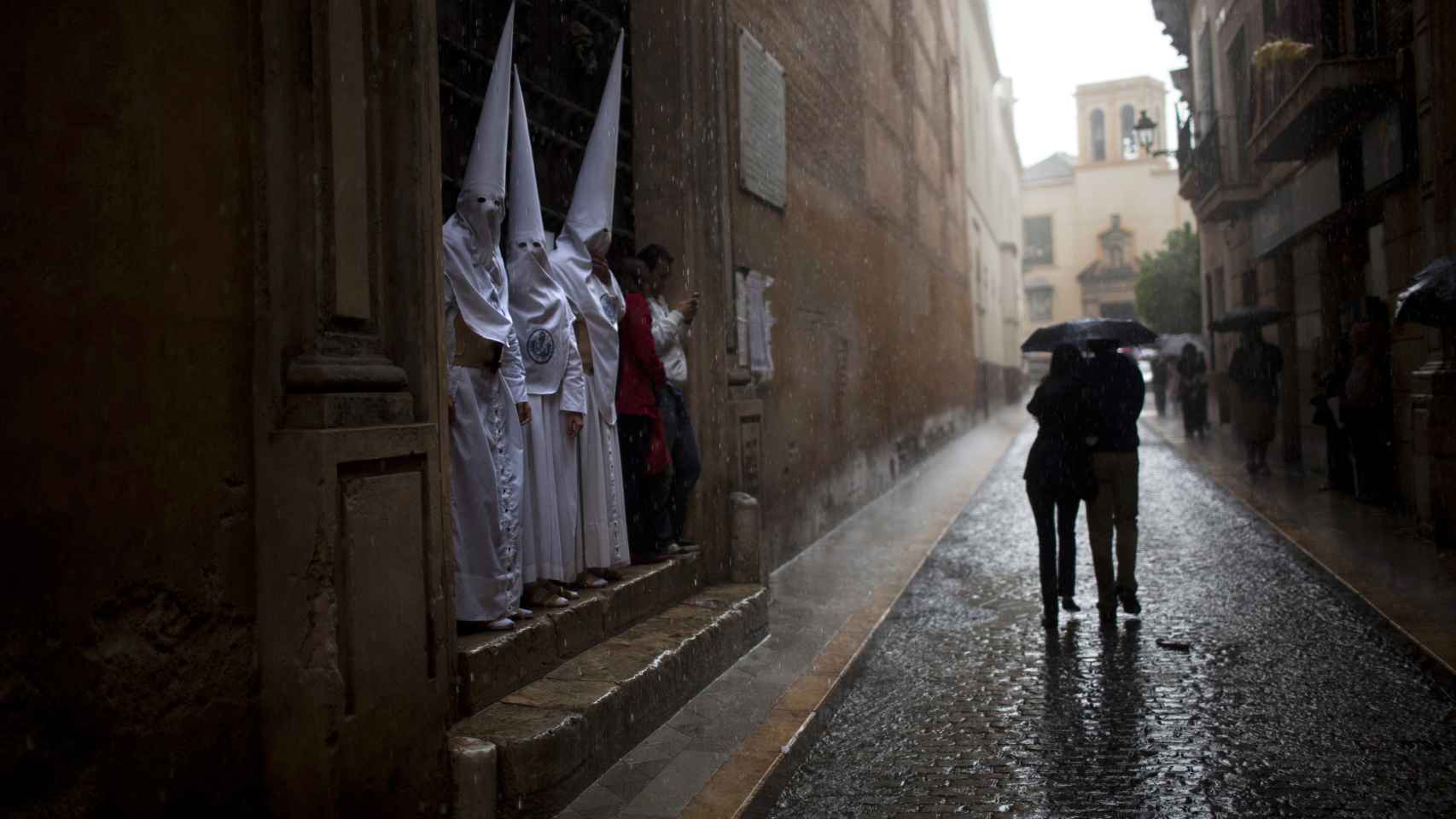 Penitentes de La Candelaria esperan a que pase la lluvia durante la Semana Santa de 2012 en Sevilla.