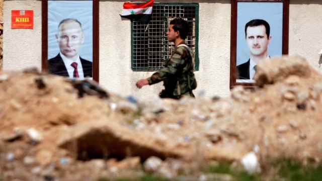 Un soldado pasa delante de los carteles del presidente de Siria y el de Rusia.