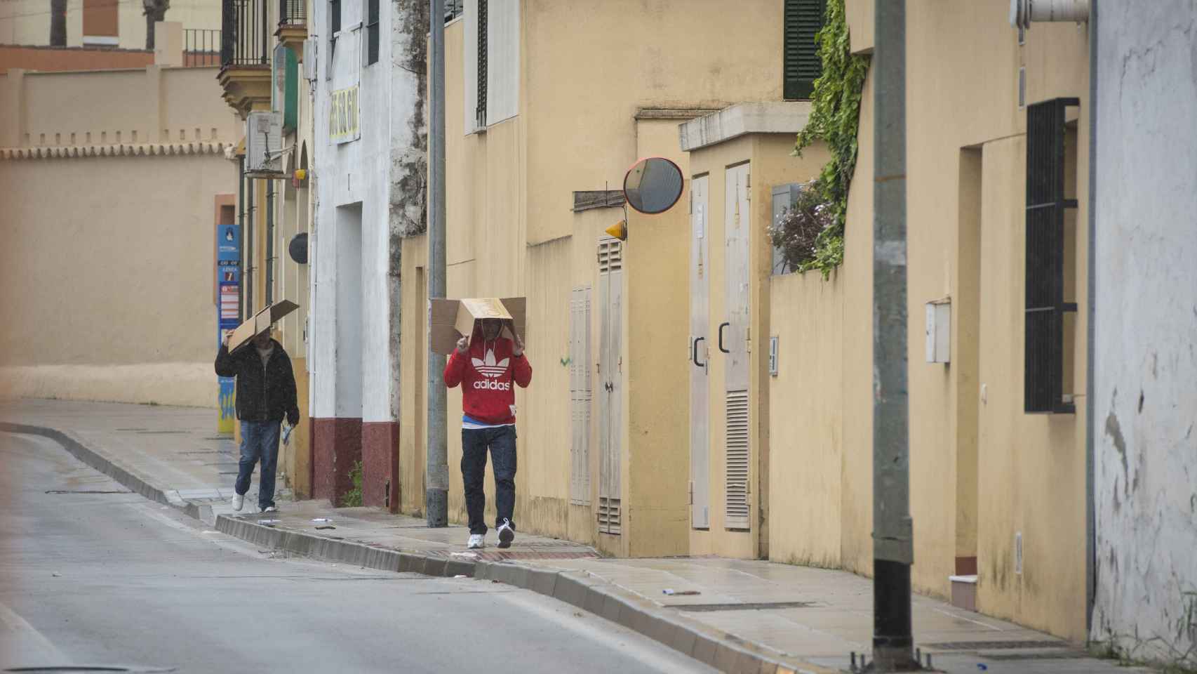 Agustín (sudadera roja) y su compañero caminan bajo un fuerte aguacero por las calles de Sanlúcar de Barrameda este pasado martes.
