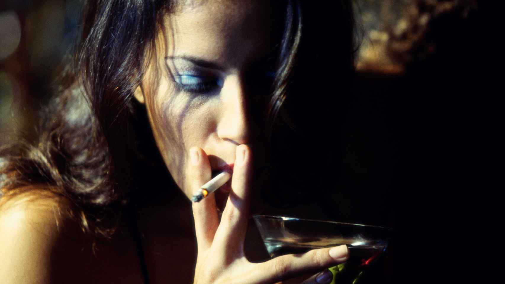 Una mujer fuma a la misma vez que sostiene una copa en su mano.