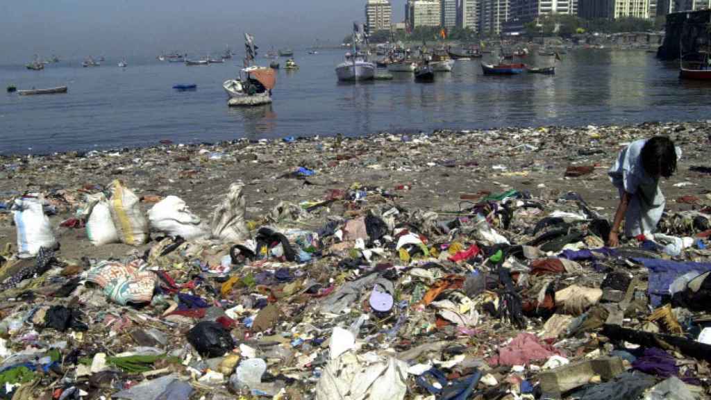 Una chica busca objetos que reciclar entre los residuos plásticos de una playa en Bombay, India.