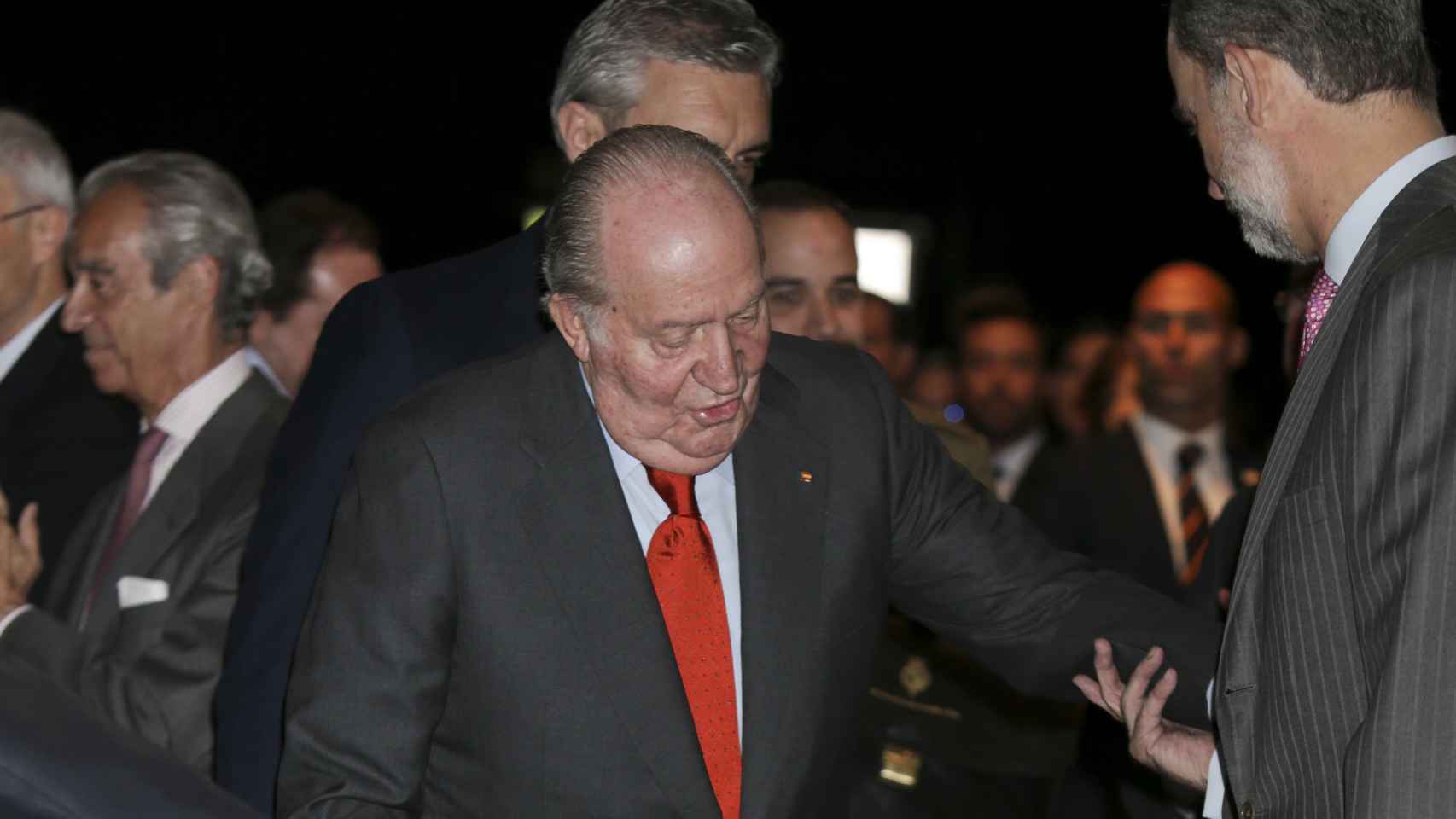 Juan Carlos I se apoya en su muleta con la ayuda de su hijo.