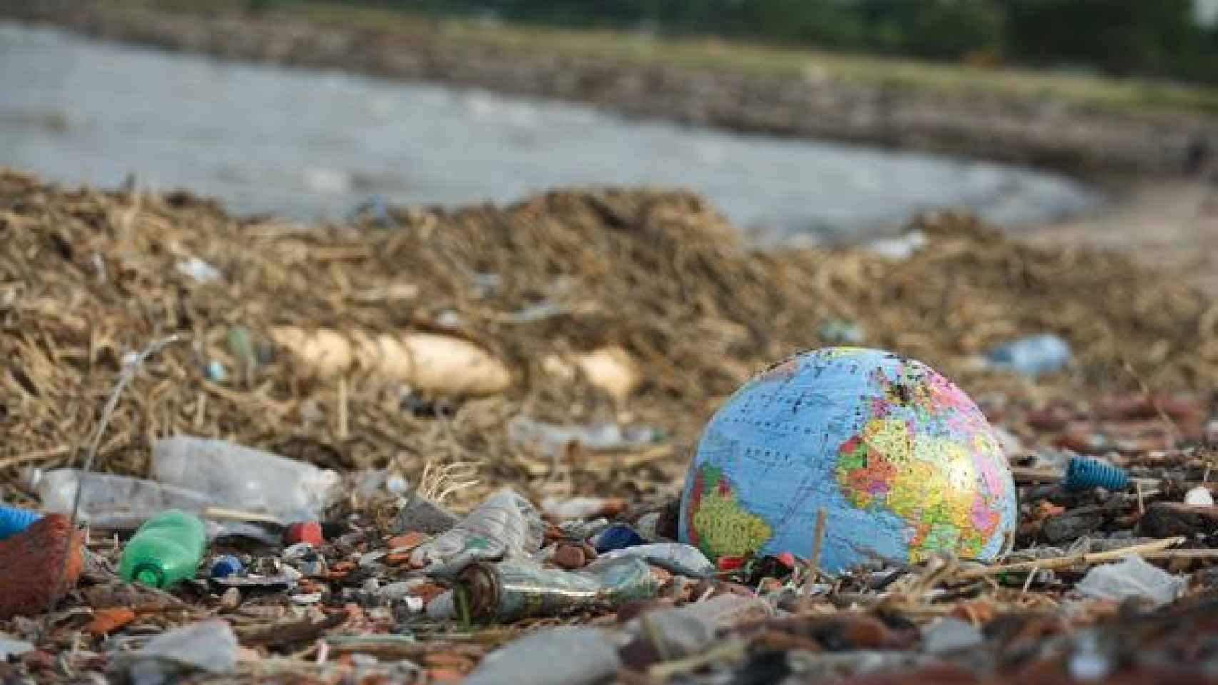 Un globo terráqueo de plástico abandonado junto a los desperdicios en la costa.