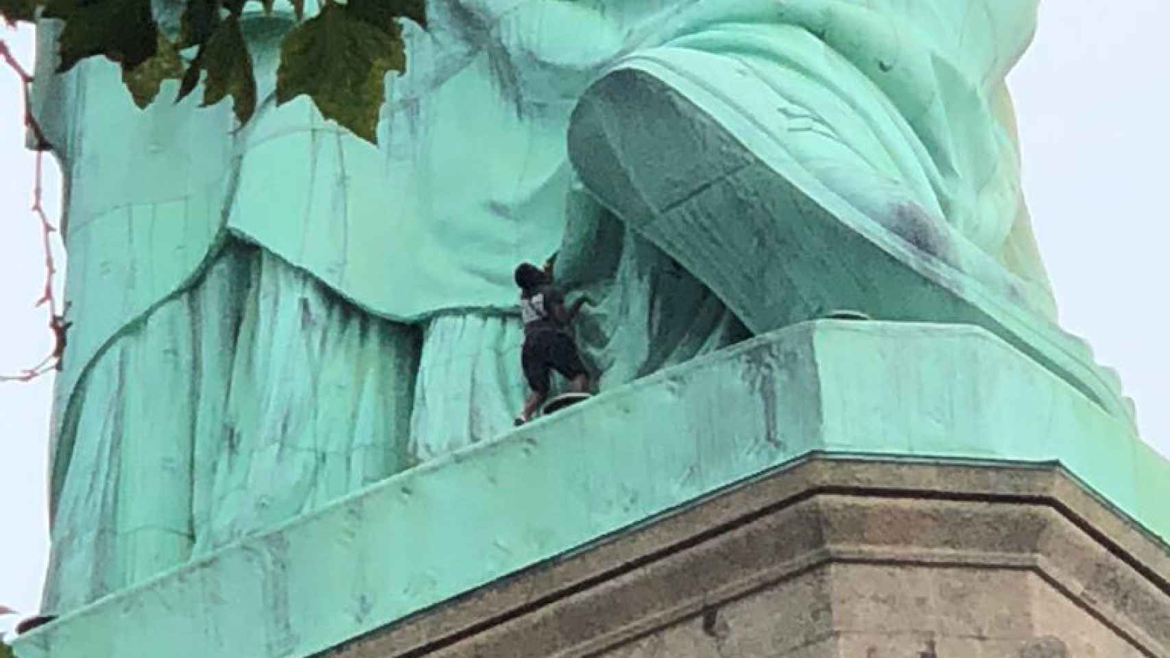 Momento en que la mujer trepa hasta el pedestal de la estatua de la Libertad.