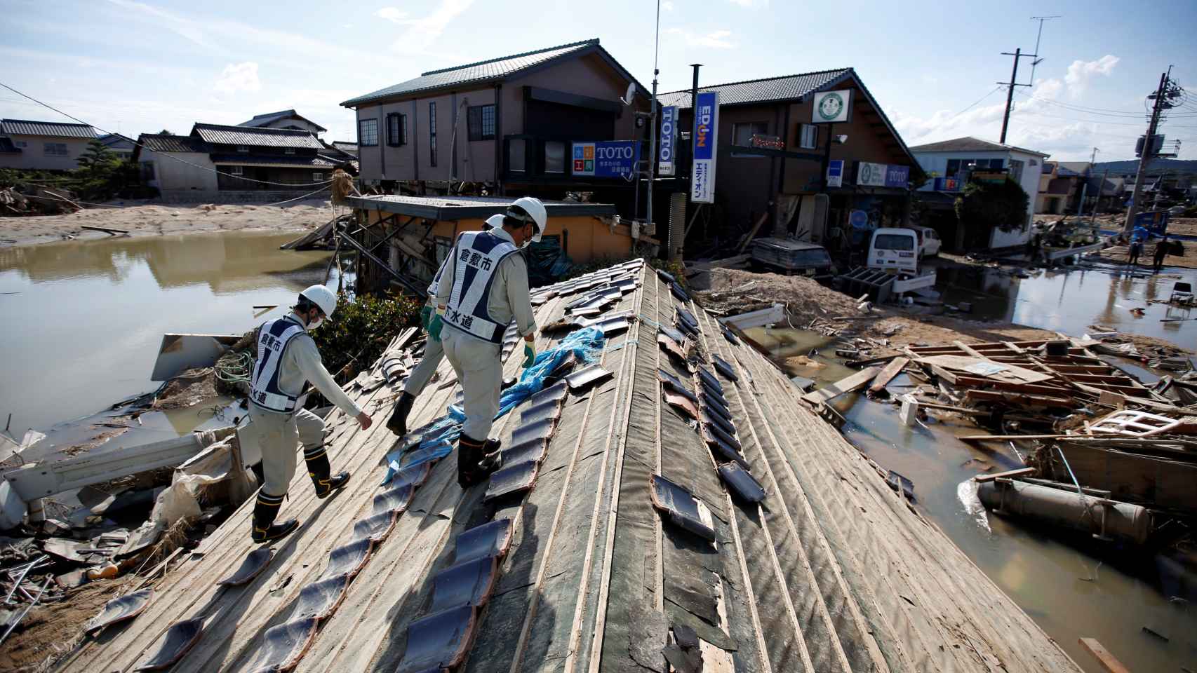 Trabajadores caminan en el techo de unas casas en busca de sobrevivientes.