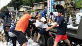 Estudiantes voluntarios retiran el lodo en sacos que cargan a un camión de la Fuerza Terrestre de Autodefensa de Japón, en Hiroshima.