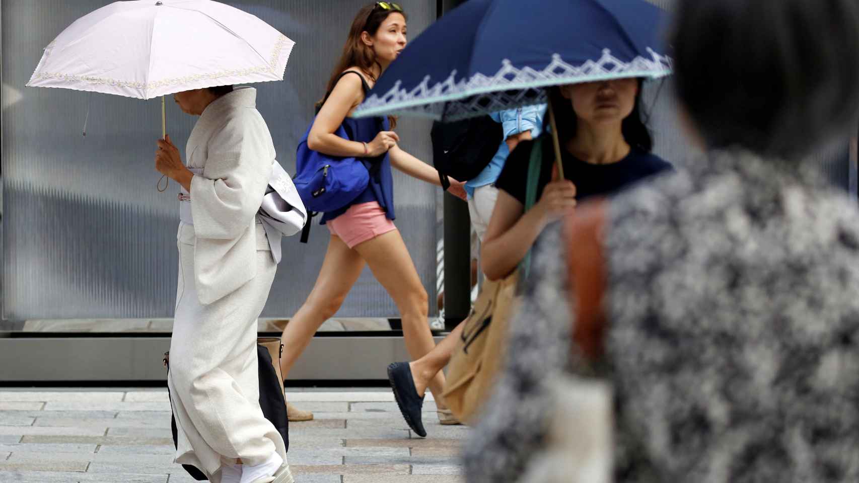 Una mujer vestida de kimono usando una sombrilla camina por una calle durante una ola de calor en Tokio.