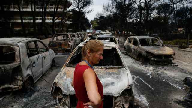 Una mujer observa los coches calcinados en las calles de la localidad griega de Mati.