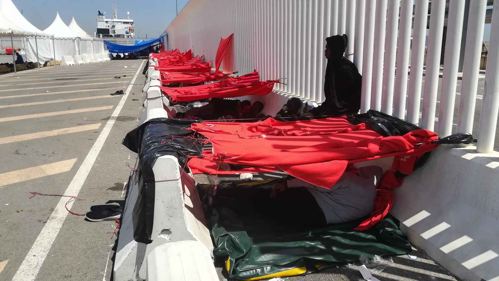 Inmigrantes se resguardan bajo mantas de Cruz Roja del calor, en el dique norte del puerto de Algeciras (Cádiz).