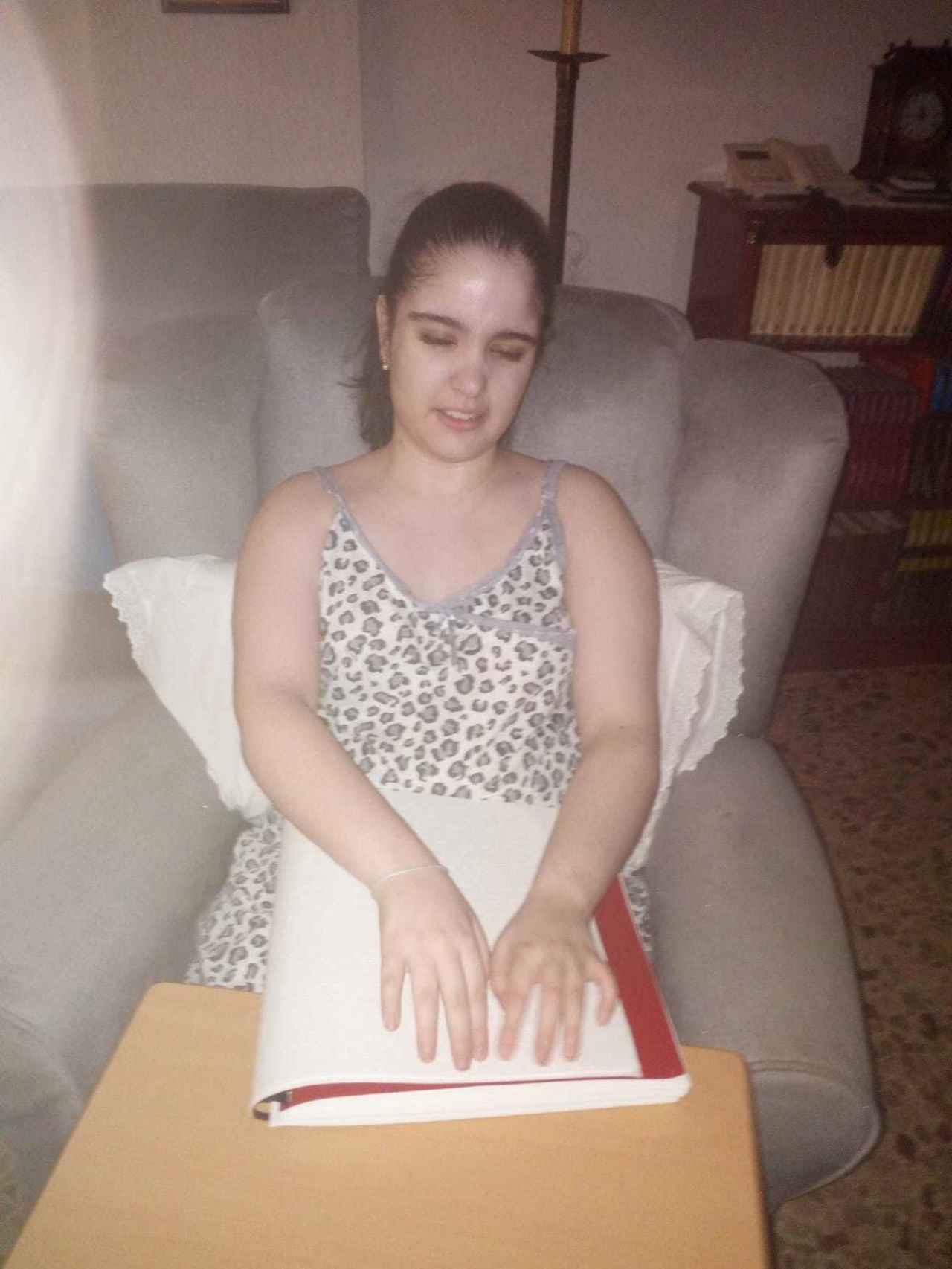 Alba, que es ciega de nacimiento, ya consigue pasar varias horas sentada en un sofá. En la imagen, tomada este miércoles en su casa, lee un libro escrito en braille.