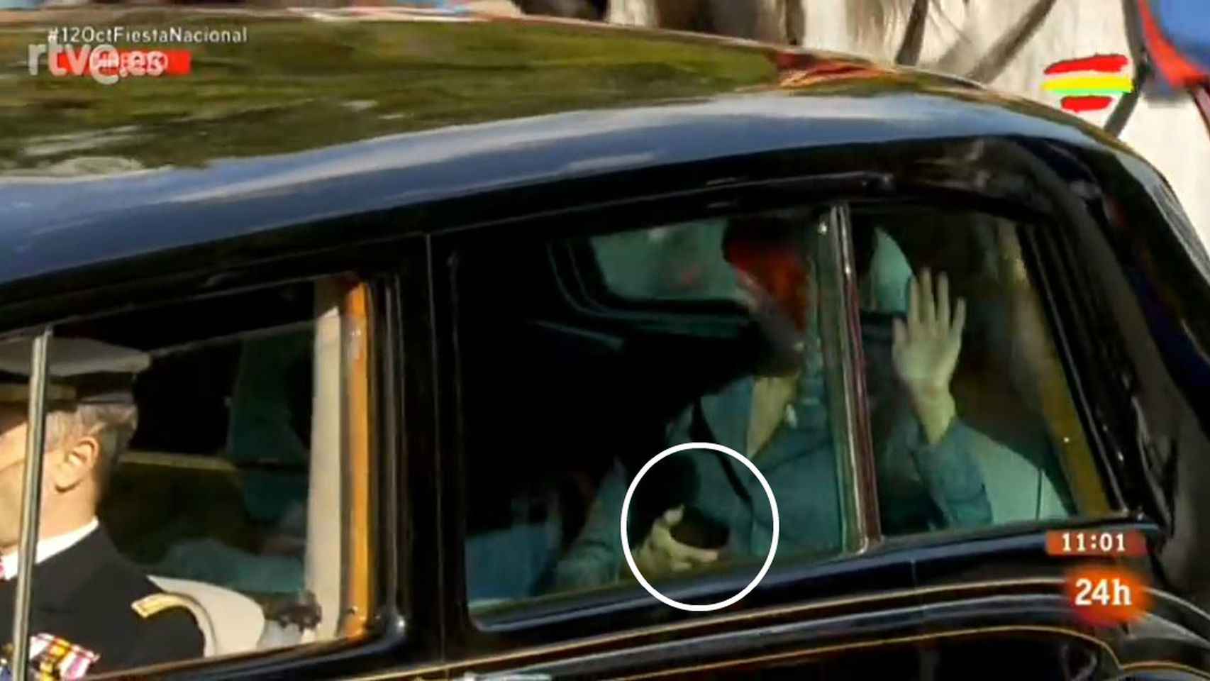 La reina Letizia utilizando su teléfono móvil y saludando con la otra mano.