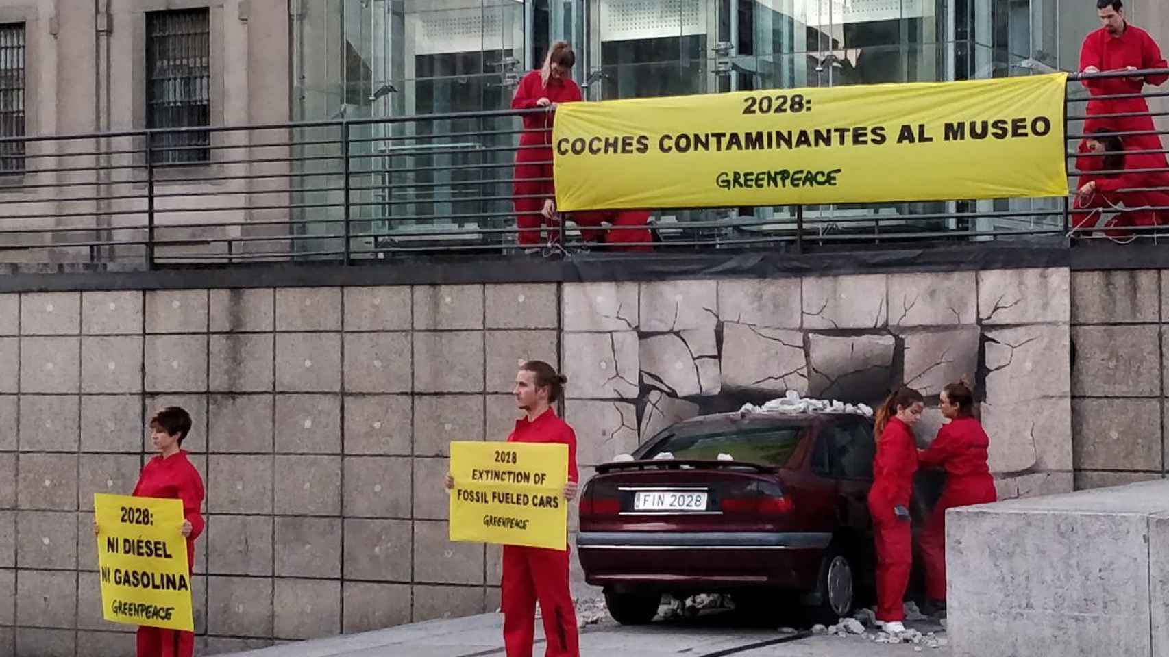 Los activistas de Greenpeace despliegan los carteles junto al coche empotrado.