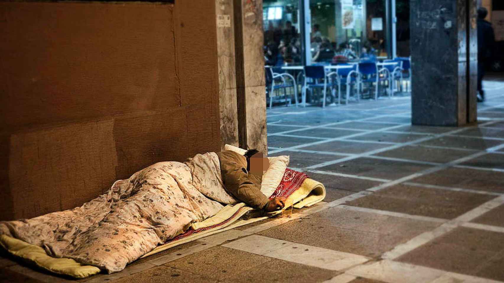 Un hombre sin techo duerme en la acera, junto a una cafetería