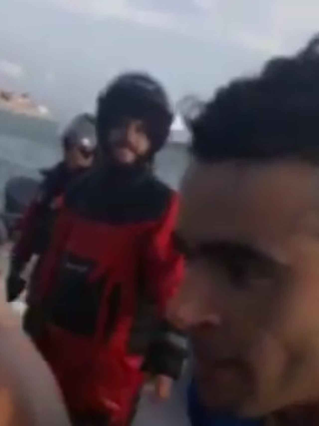 En esta captura de imagen se observa, con casco y ropa impermeable, a un narcotraficante mientras observa cómo los inmigrantes se lanzan al mar al llegar a la orilla de la playa.