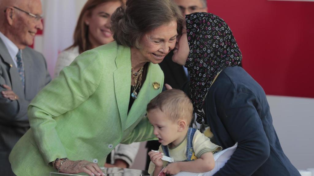 La reina Sofía da recibe dos besos a una señora y su hijo pequeño.