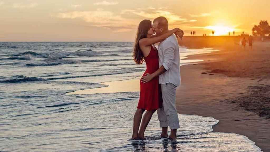 Una pareja de tortolitos se besa apasionadamente en una paradisíaca playa al atardecer