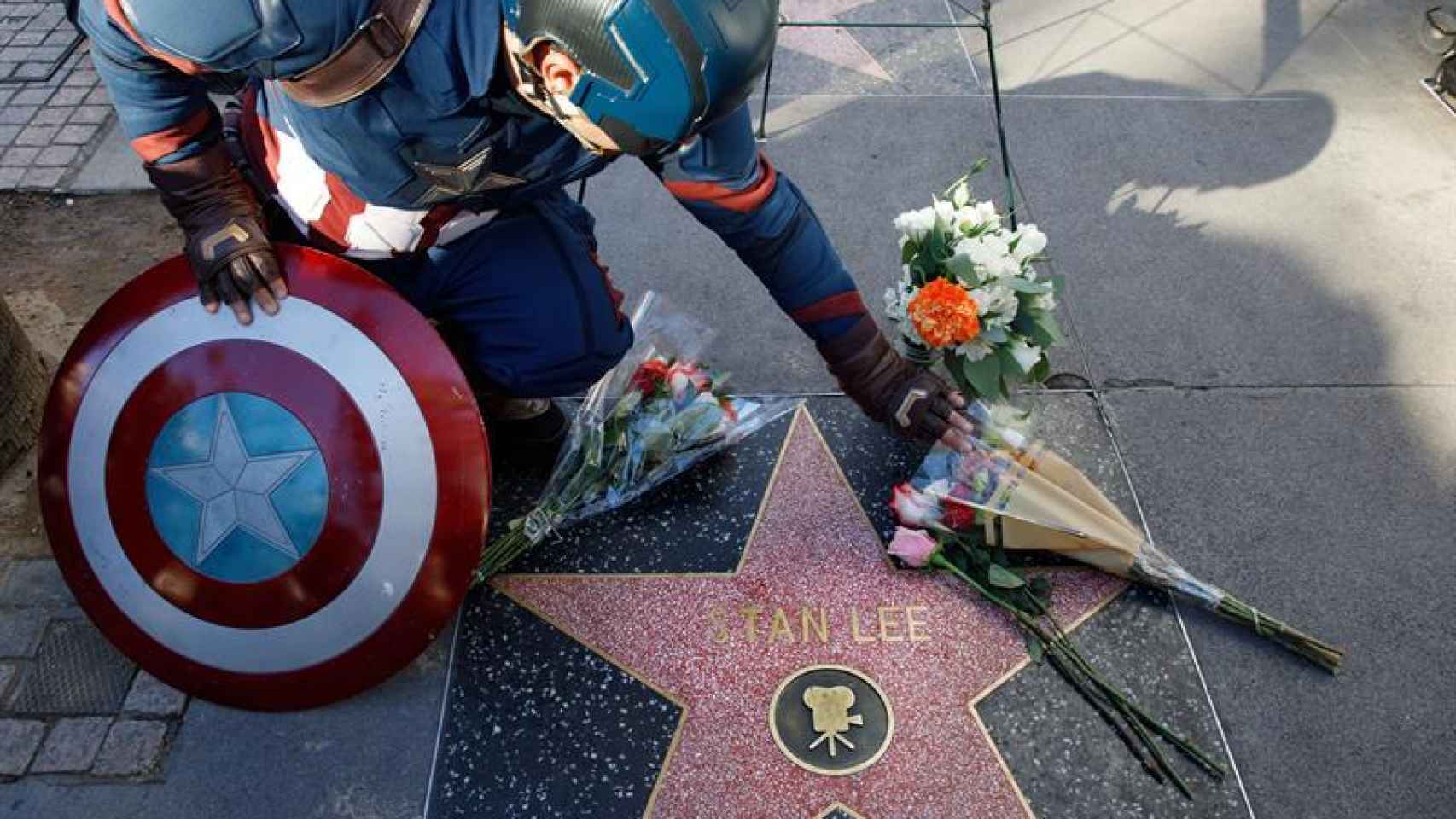 Un hombre vestido de Capitán América deja flores en la estrella de Stan Lee.