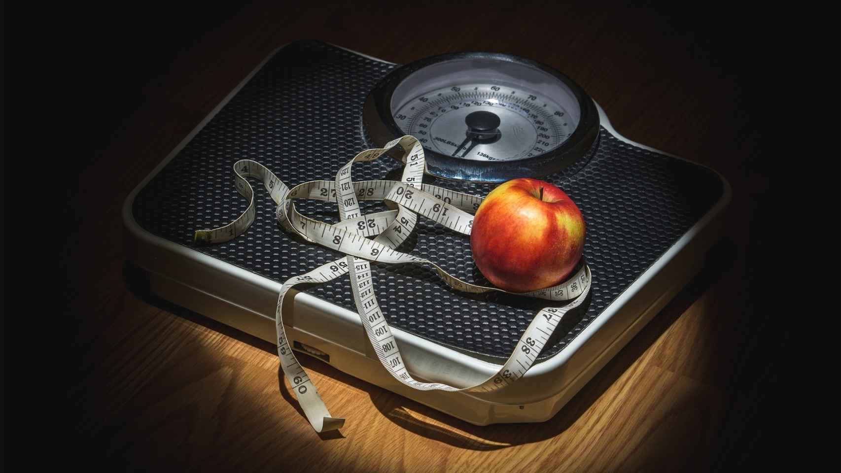 Una manzana rodeada por una cinta métrica encima de una báscula.