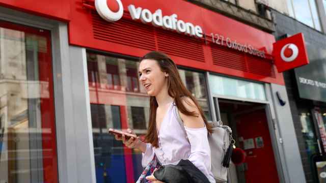 FILE PHOTO: A woman holds a phone as she passes a Vodafone  store in London